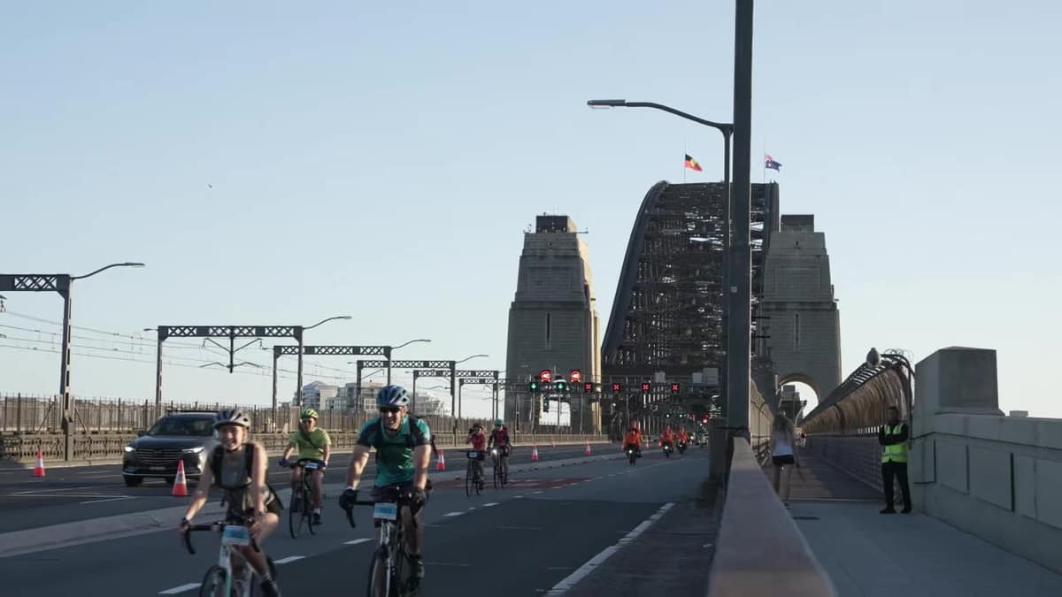 Cyclists riding across the Sydney Harbour Bridge, the arch rising behind them.