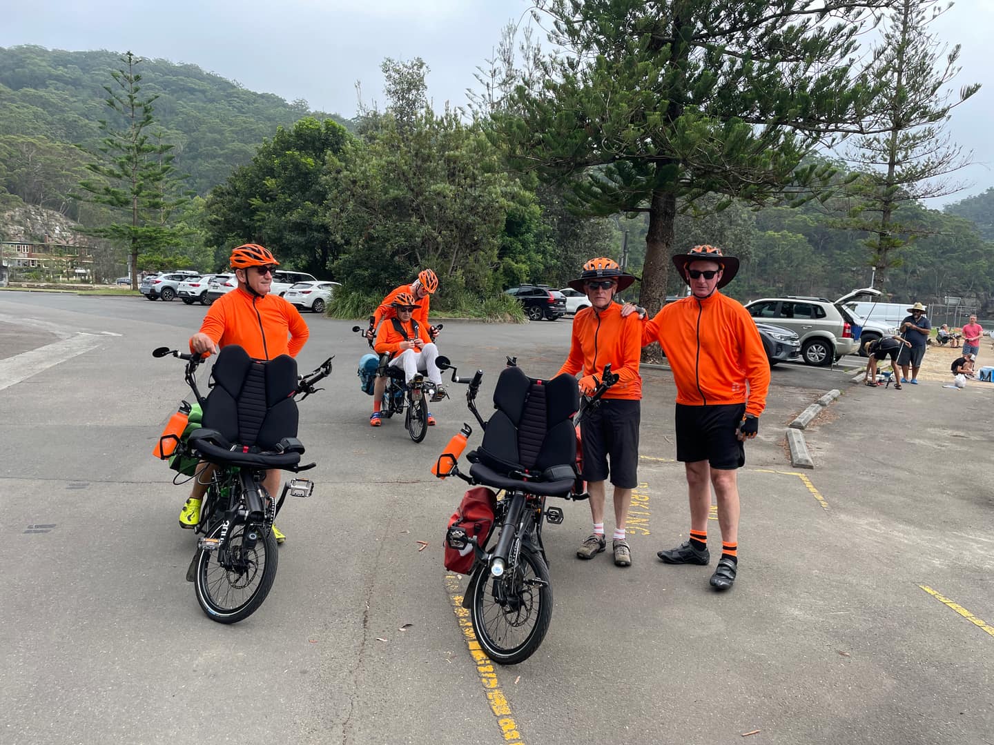 Five cyclists in bright orange Riding Together jerseys taking a break.