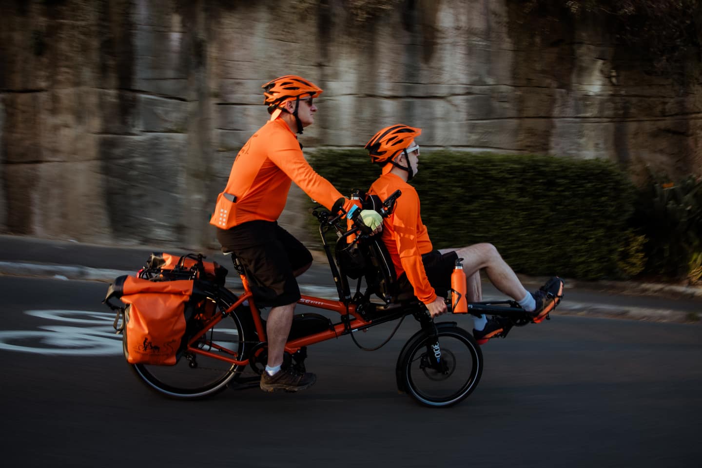 Two riders in bright orange jerseys enjoying a waterside coffee after a big ride.