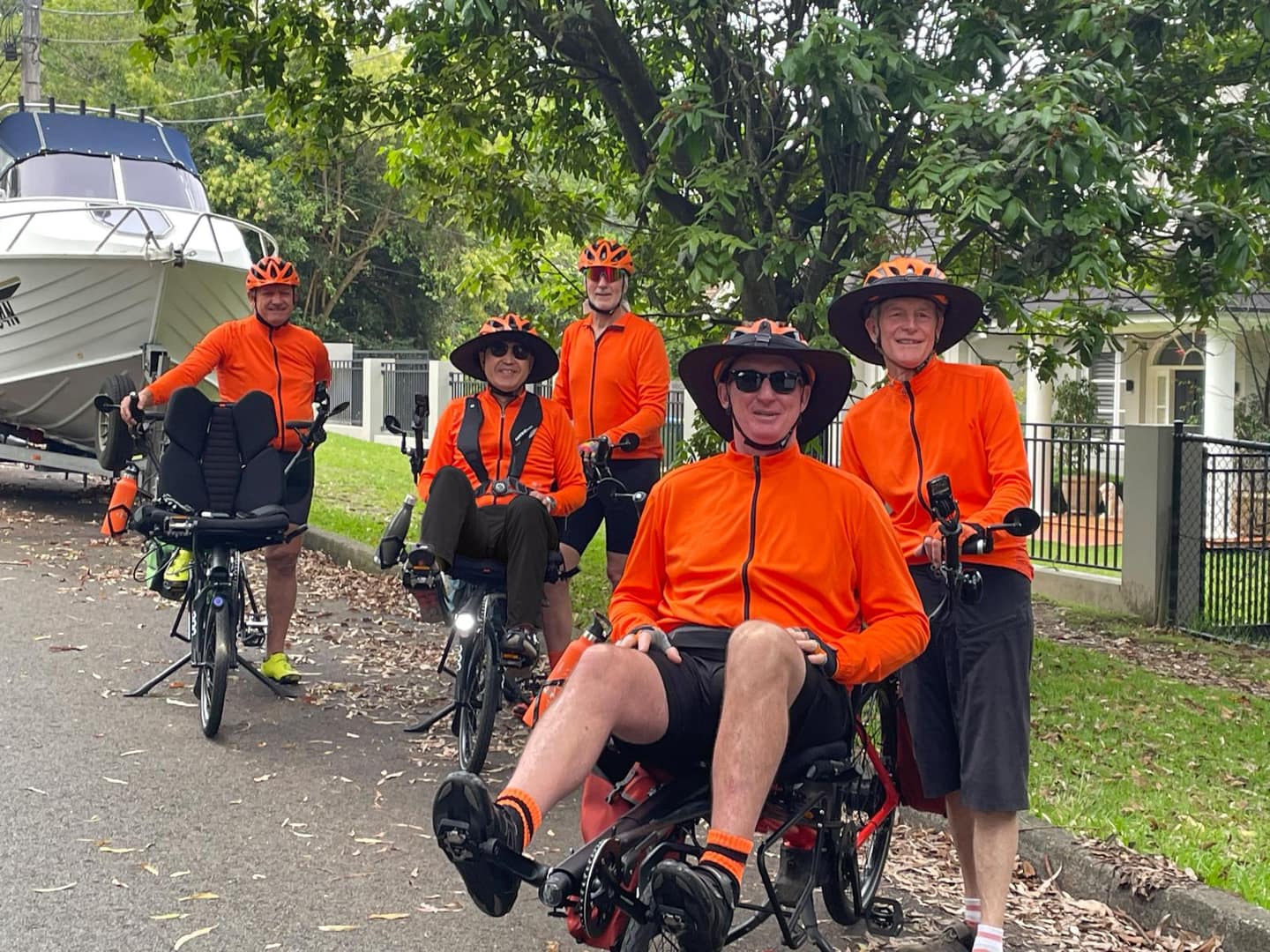 A happy team of riders and pilots wearing bright orange cycling jerseys.